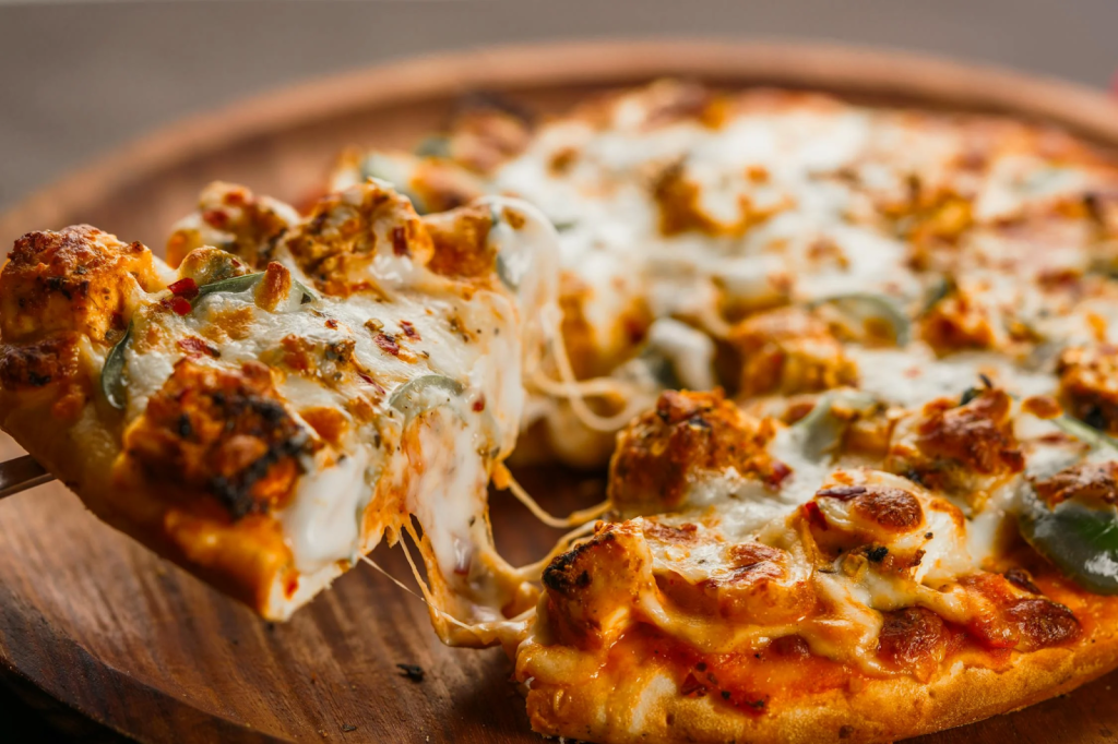 Close-up of a slice of cheese pizza with melted mozzarella, chunky toppings, and crispy crust